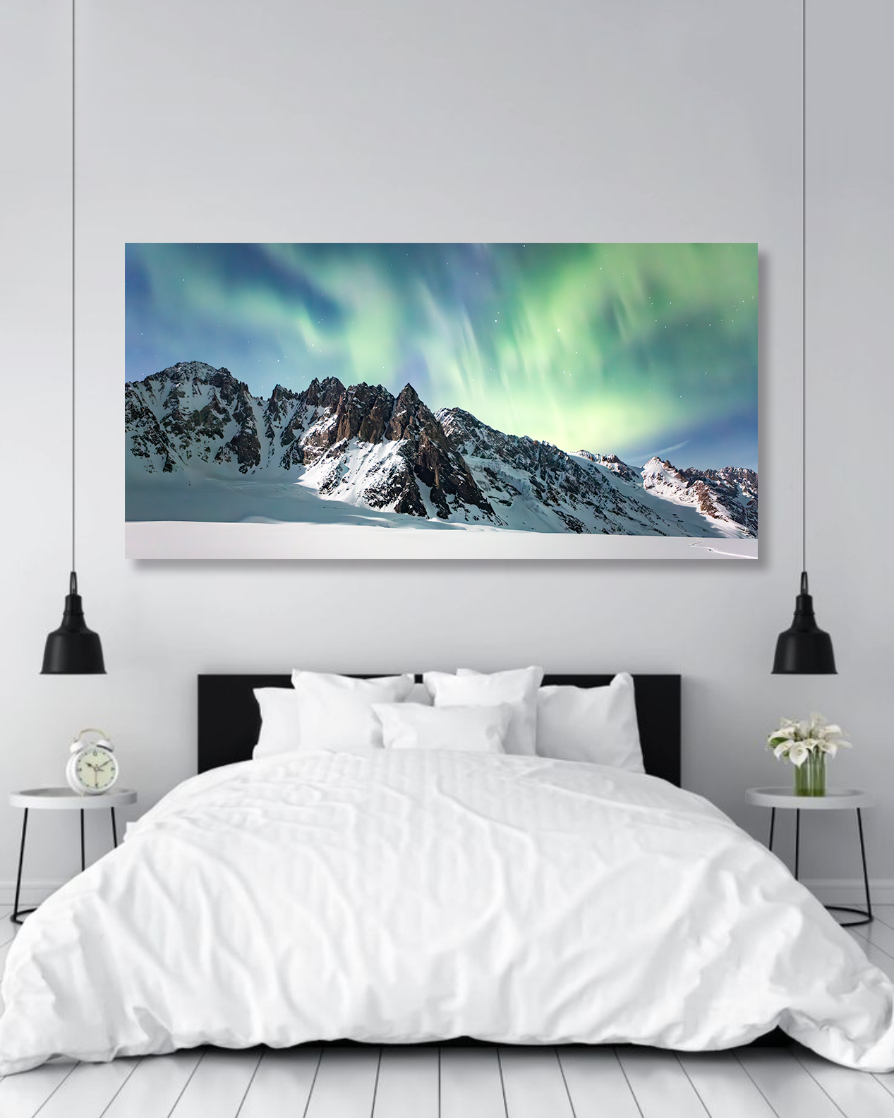A fine arts photo of Aurora Borealis above the rough peaks of Alaska hang on the wall of a master bedroom.