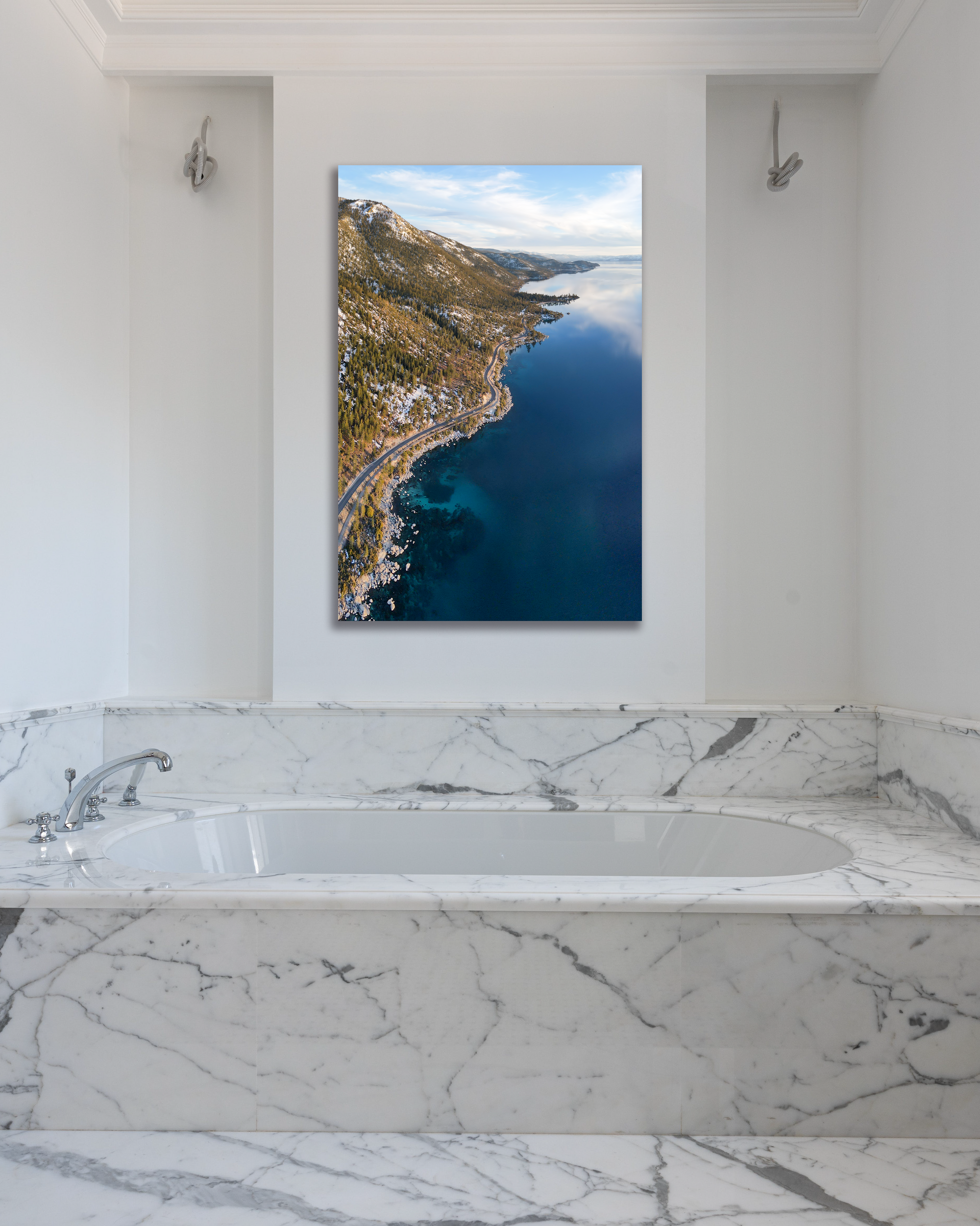 The blue waters of Lake Tahoe hug the shoreline of the a mountain landscape in a fine arts photo hanging above a marble bathtub.