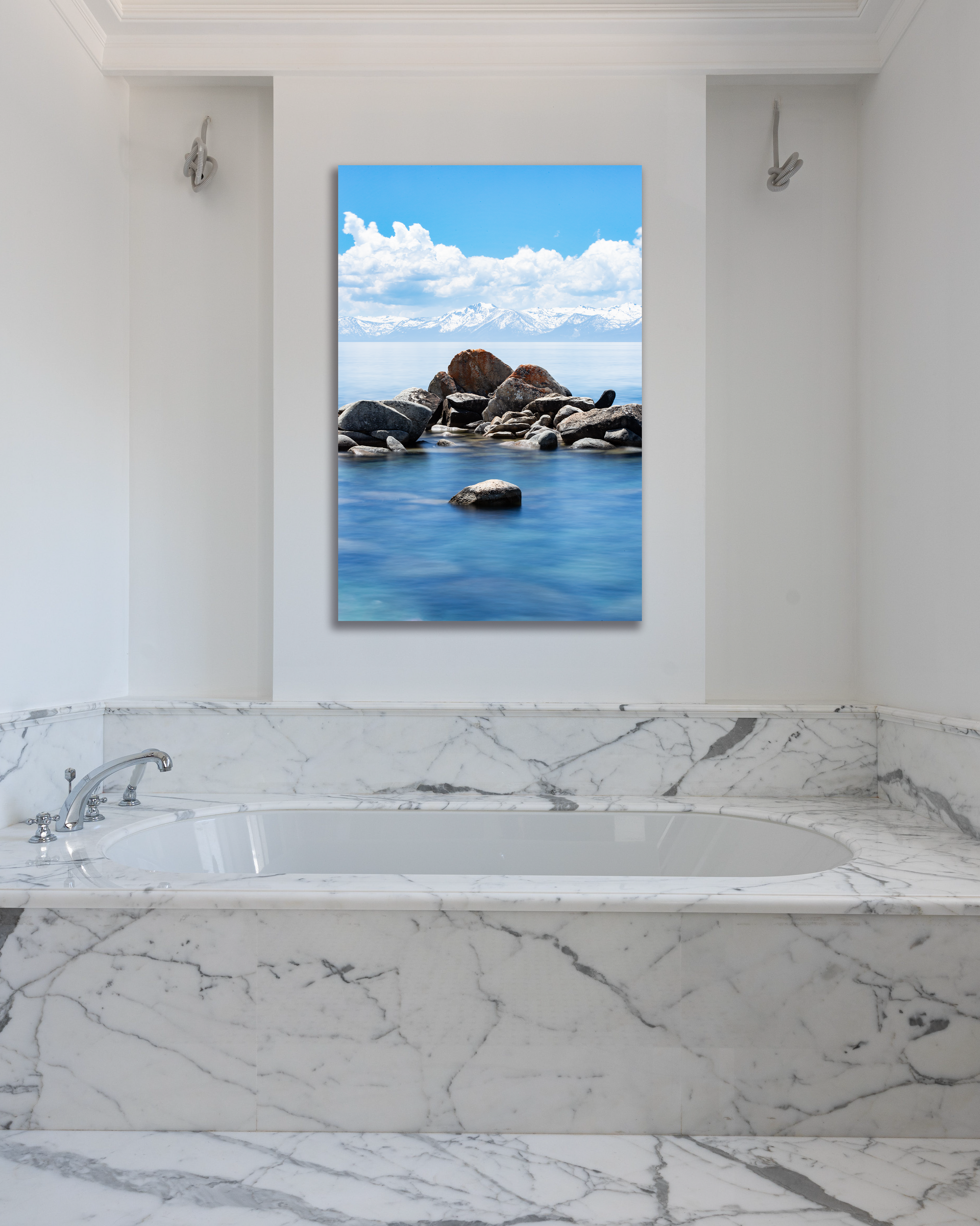 The crystal blue waters of Lake Tahoe lap against a cluster of rocks in a fine arts photograph hanging above a marbled tub.