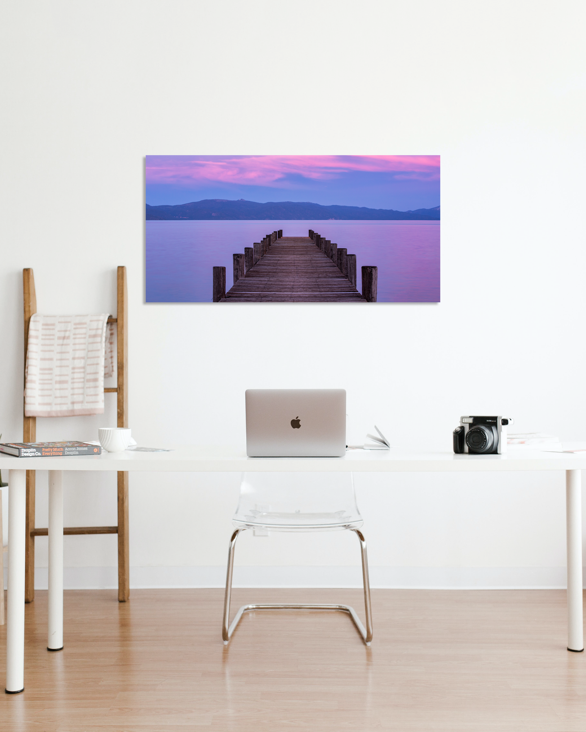 A photo of a dock jutting out into a lake during a vibrant pink and purple sunset hangs on an office wall.