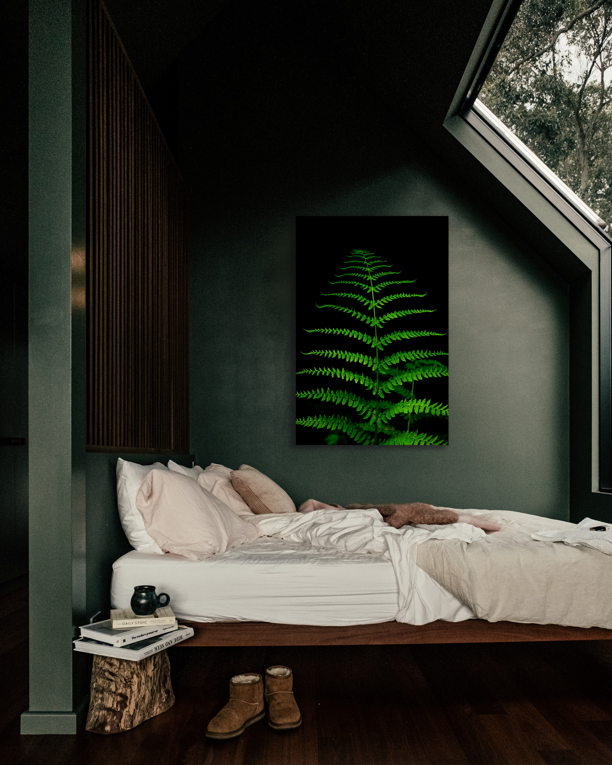 An image of a vibrant fern hangs above an unmade bed.