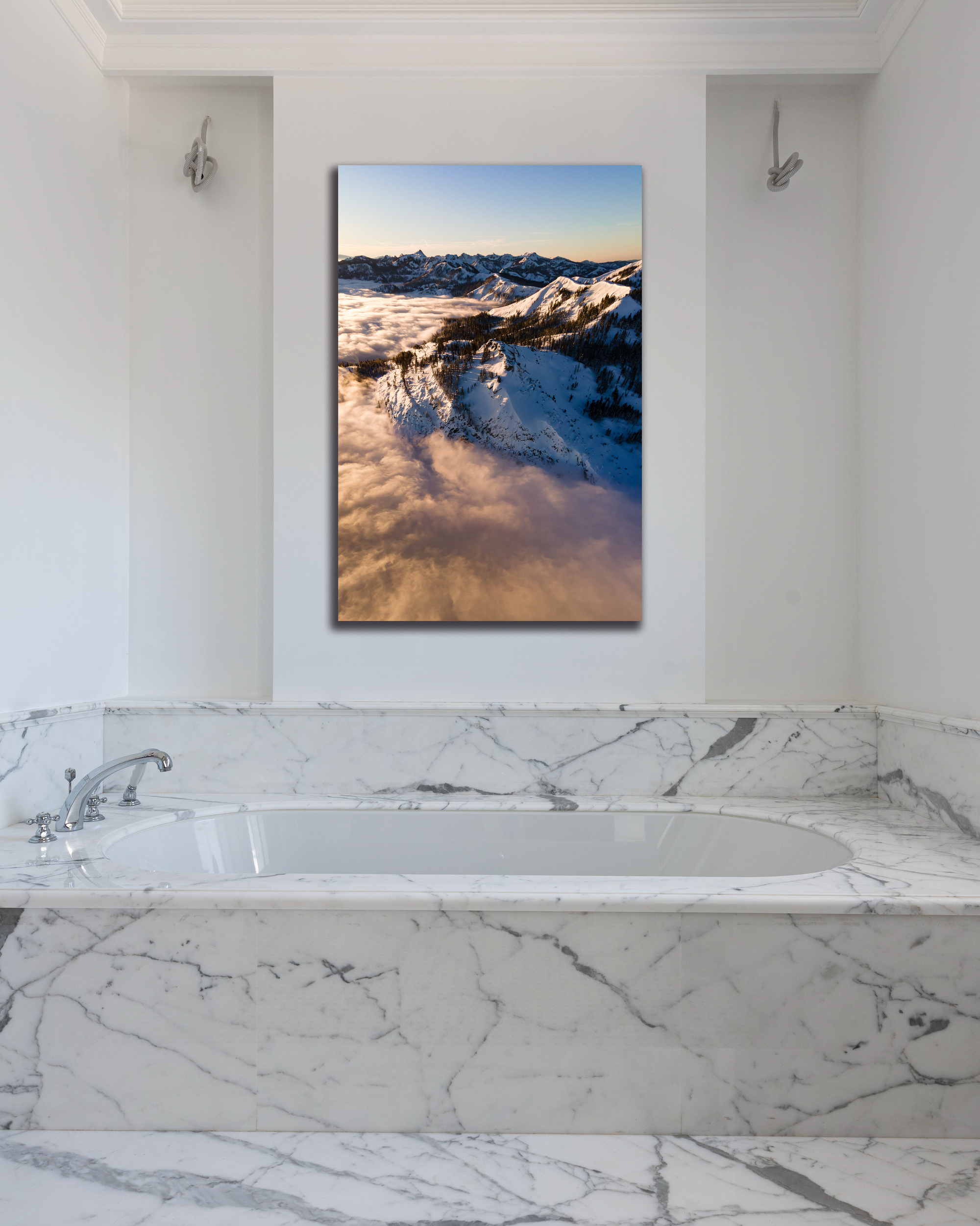 A golden hued photo of snowy mountains hang above a bathtub.