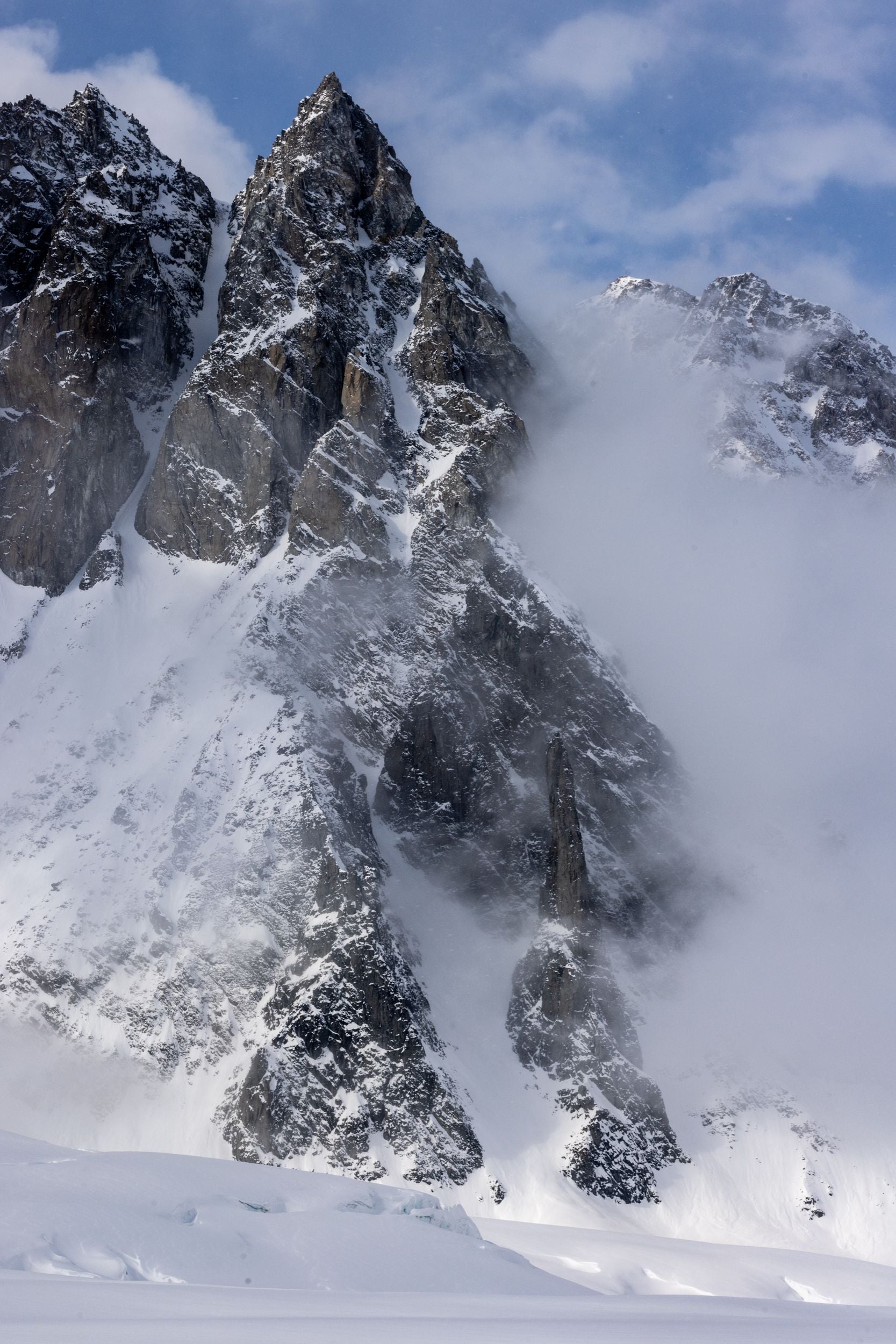 Fog pushes up towards a blue sky between mountain peaks.