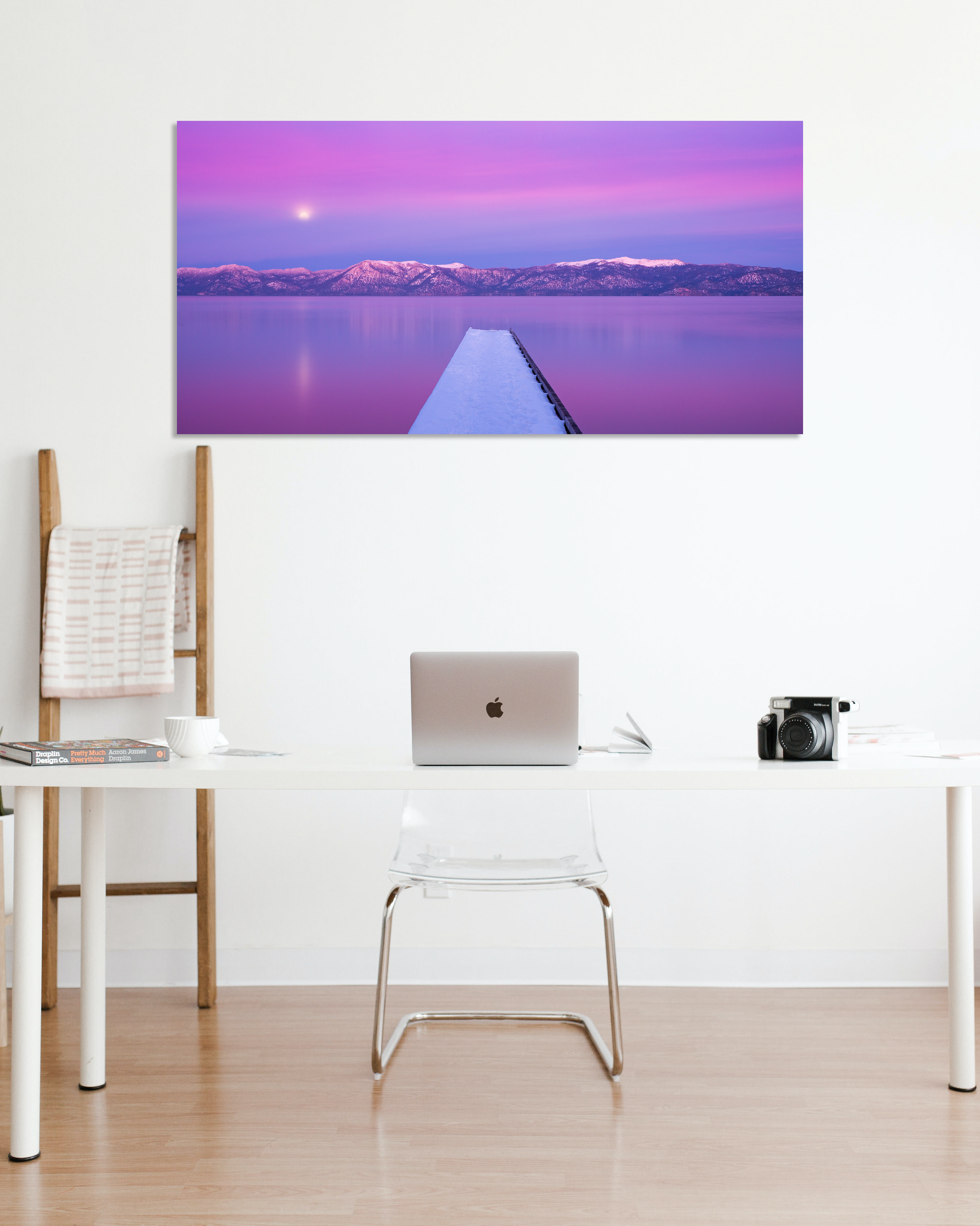 An image of snow covered dock juts out into a lake surrounded by snowcapped mountains during a moonrise hangs on a white wall.