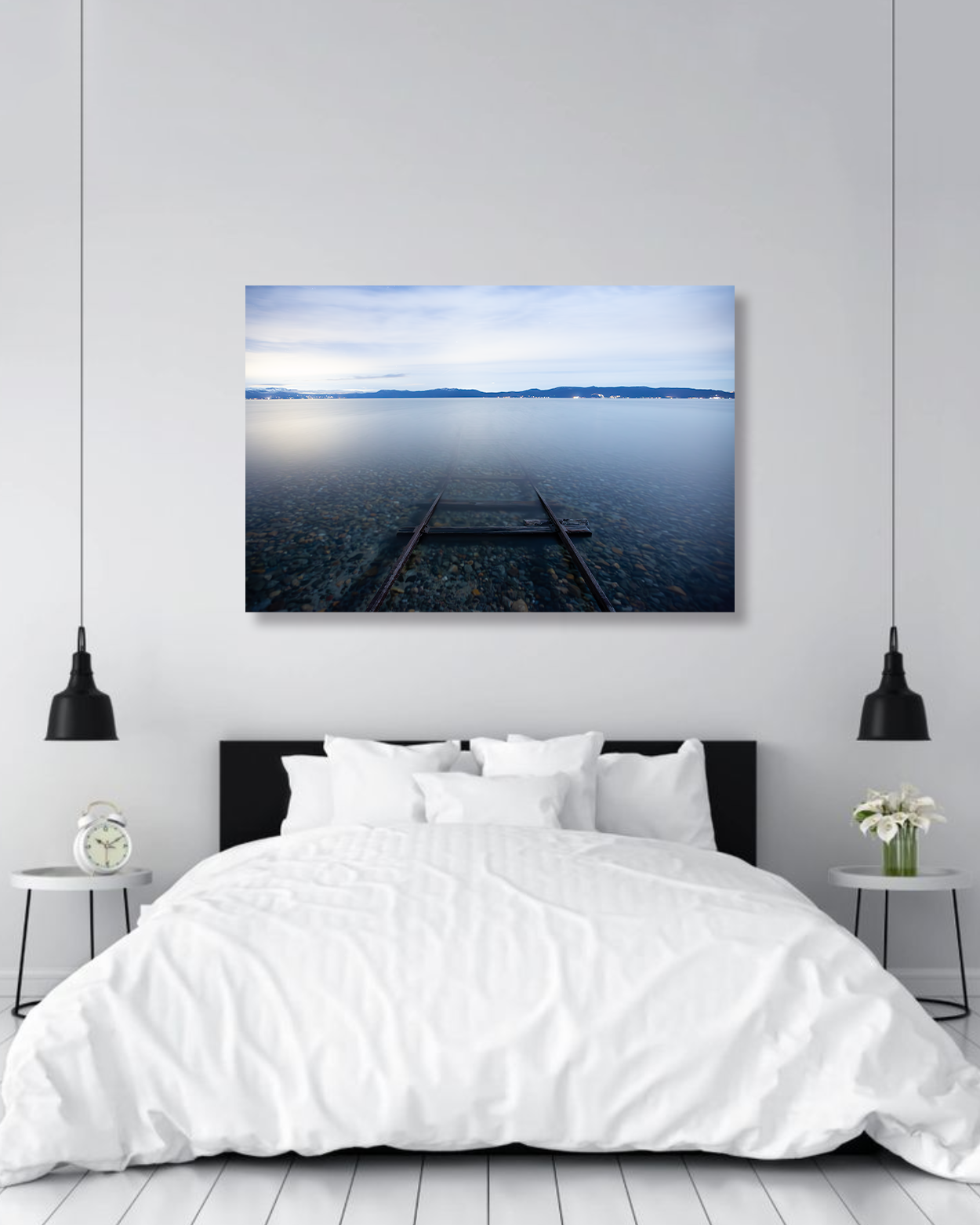 A photograph showing train tracks disappearing into a lake hang above a bed in a master bedroom.