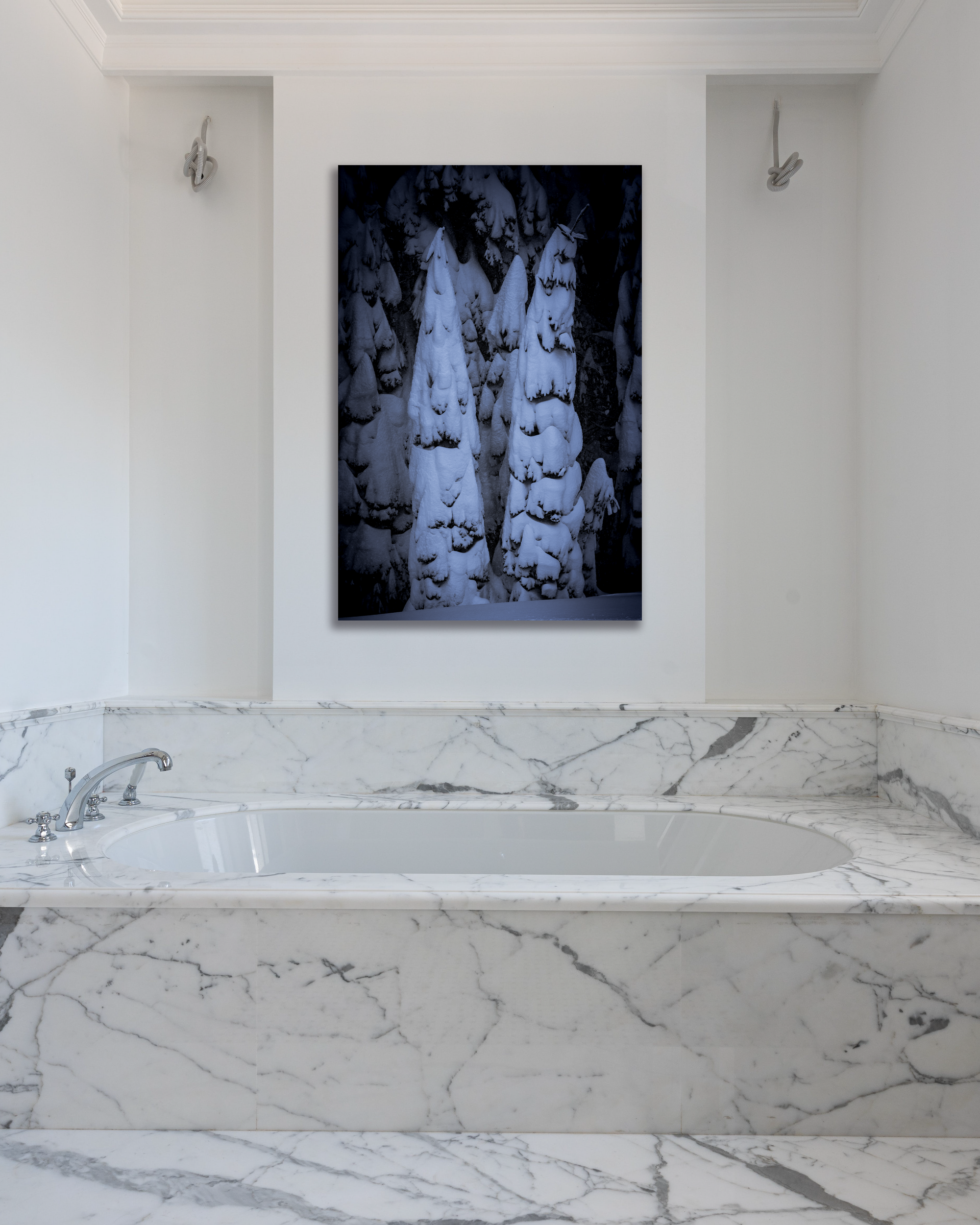 The wall of a marbled bathroom is decorated with a photo of a group of pine trees heavy with fresh snow.