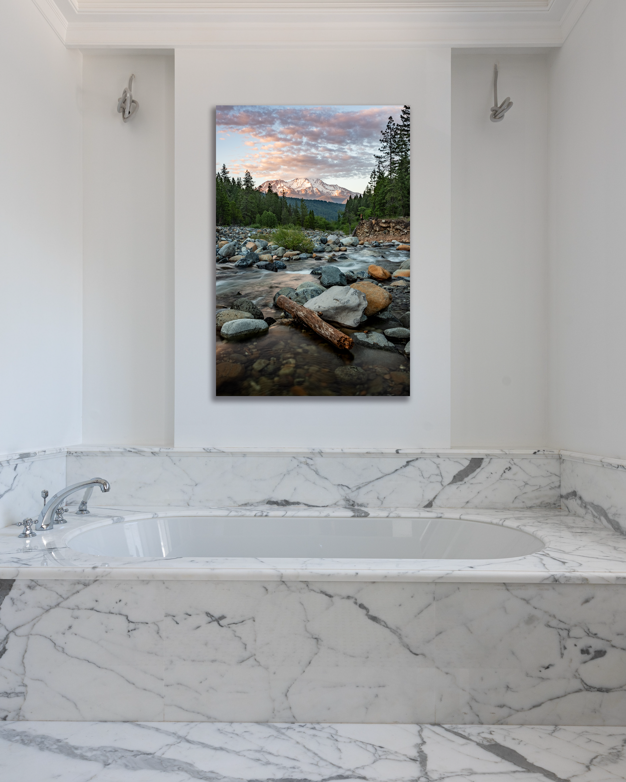 A river and mountain scape photograph hangs above a marbled bathtub.