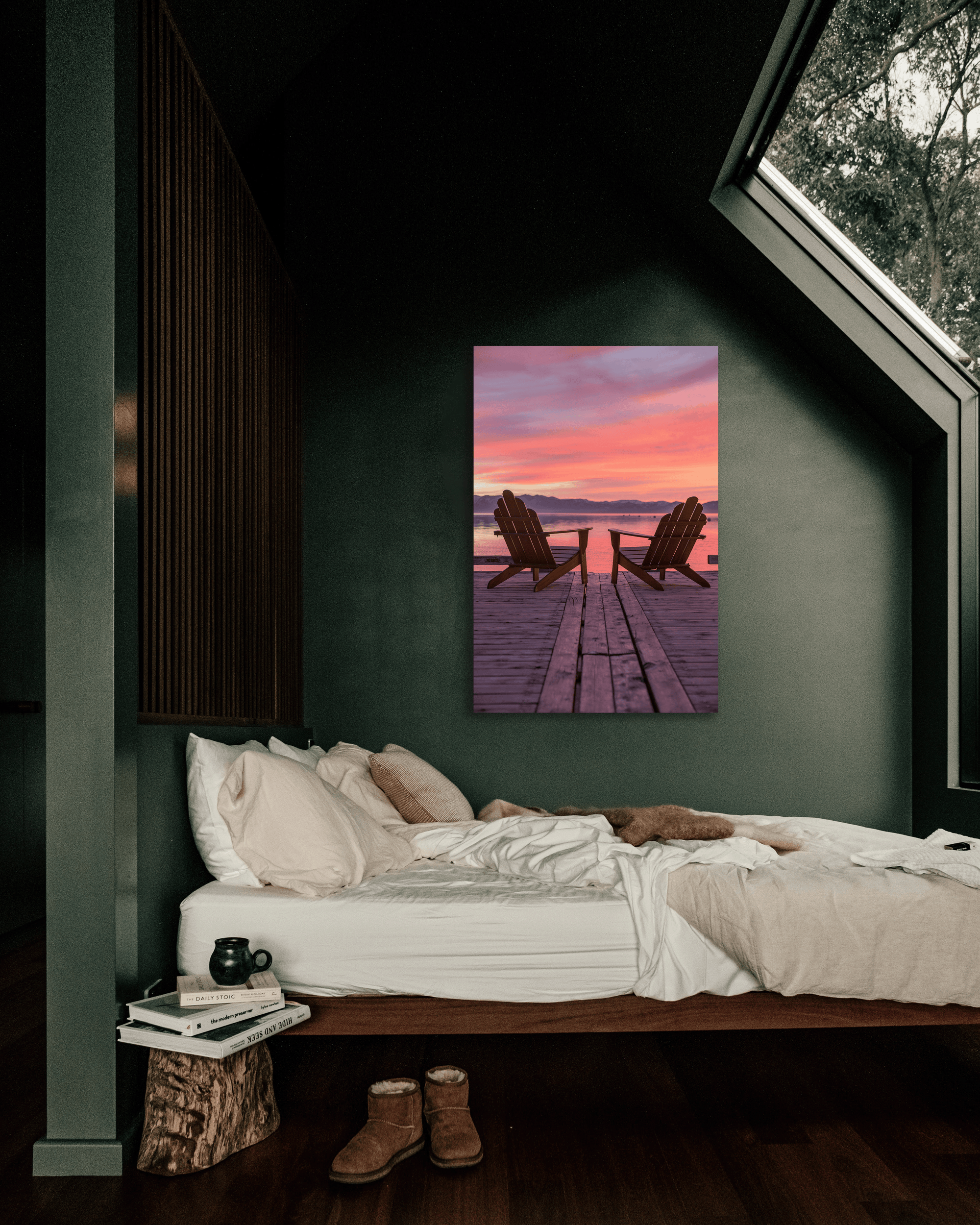 A photograph showing two Adirondack chairs on a lake dock at sunset hang above a bed on a green wall.