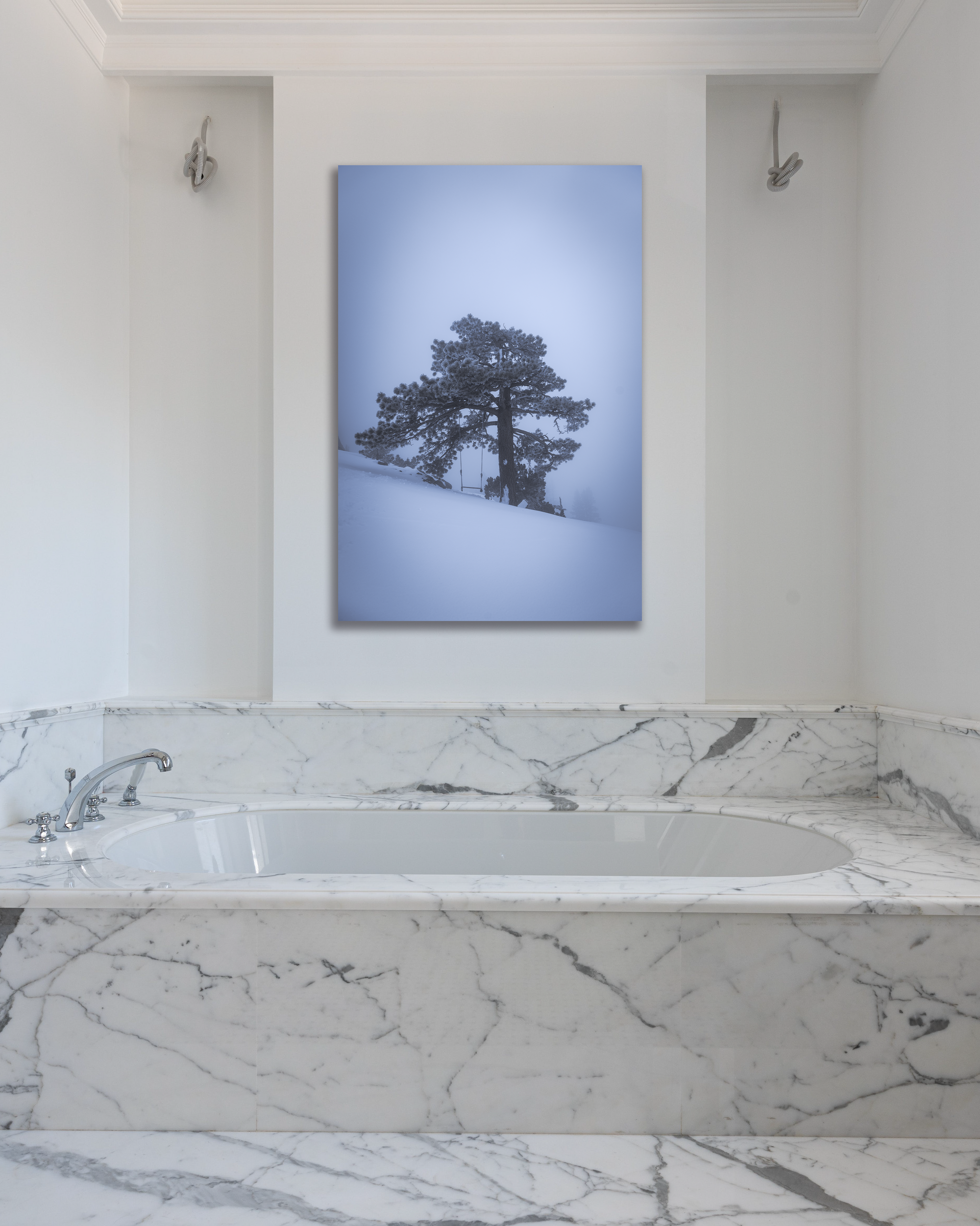 The wall of a bathroom is decorated with a photograph of a winter scape of a single tree.