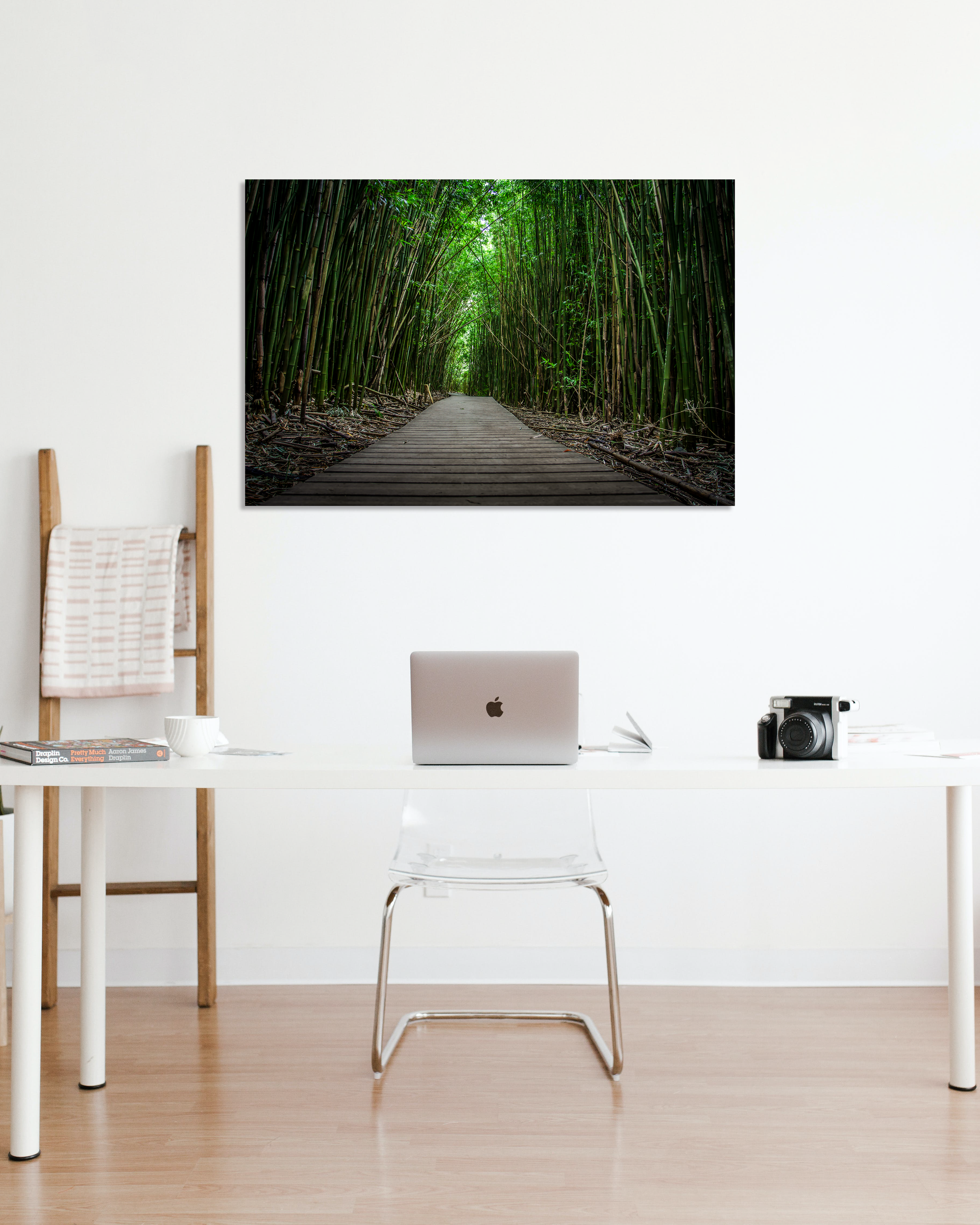 A fine art photo of a bamboo lined wooden walk way hangs above a desk on a white wall.