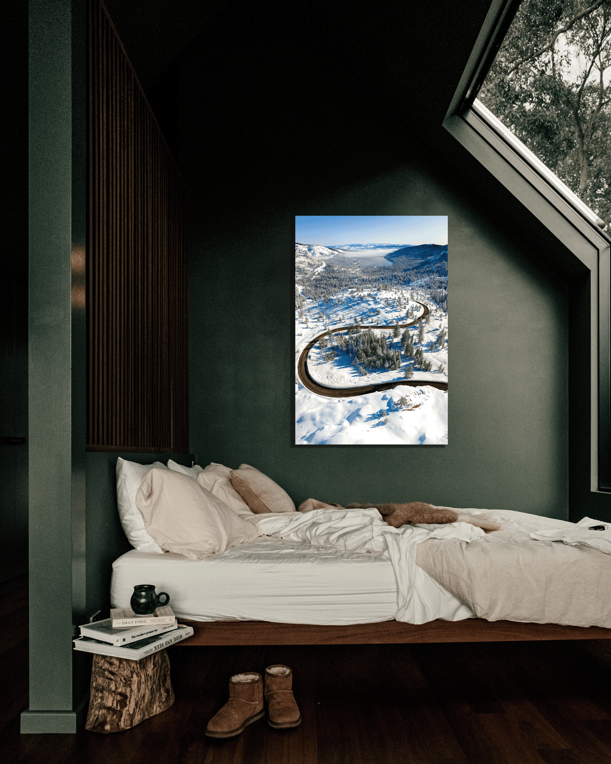 A green bedroom wall is decorated with a photo showing a highway winding down a snowy tree laden hillside towards a lake.