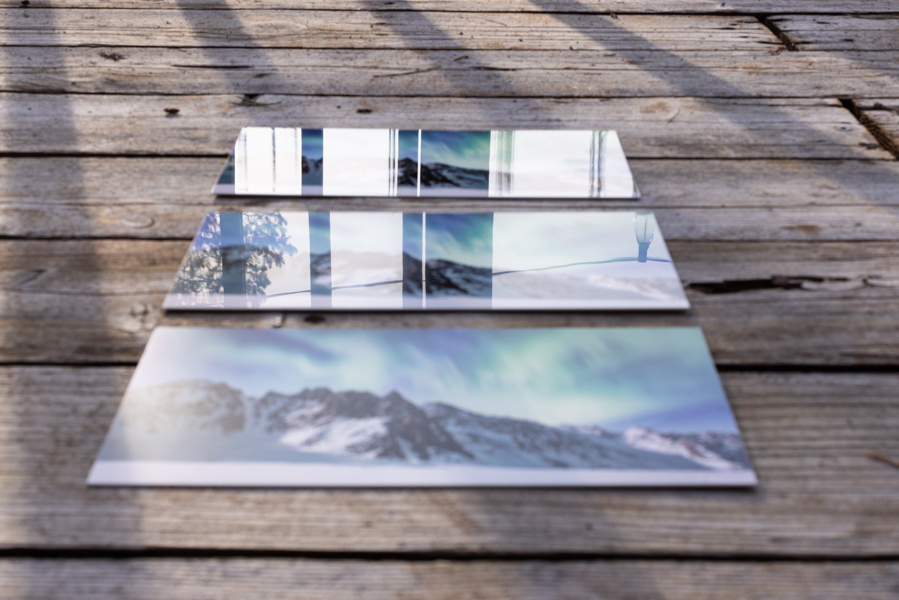 Three fine art photography prints lay on a wooden deck.