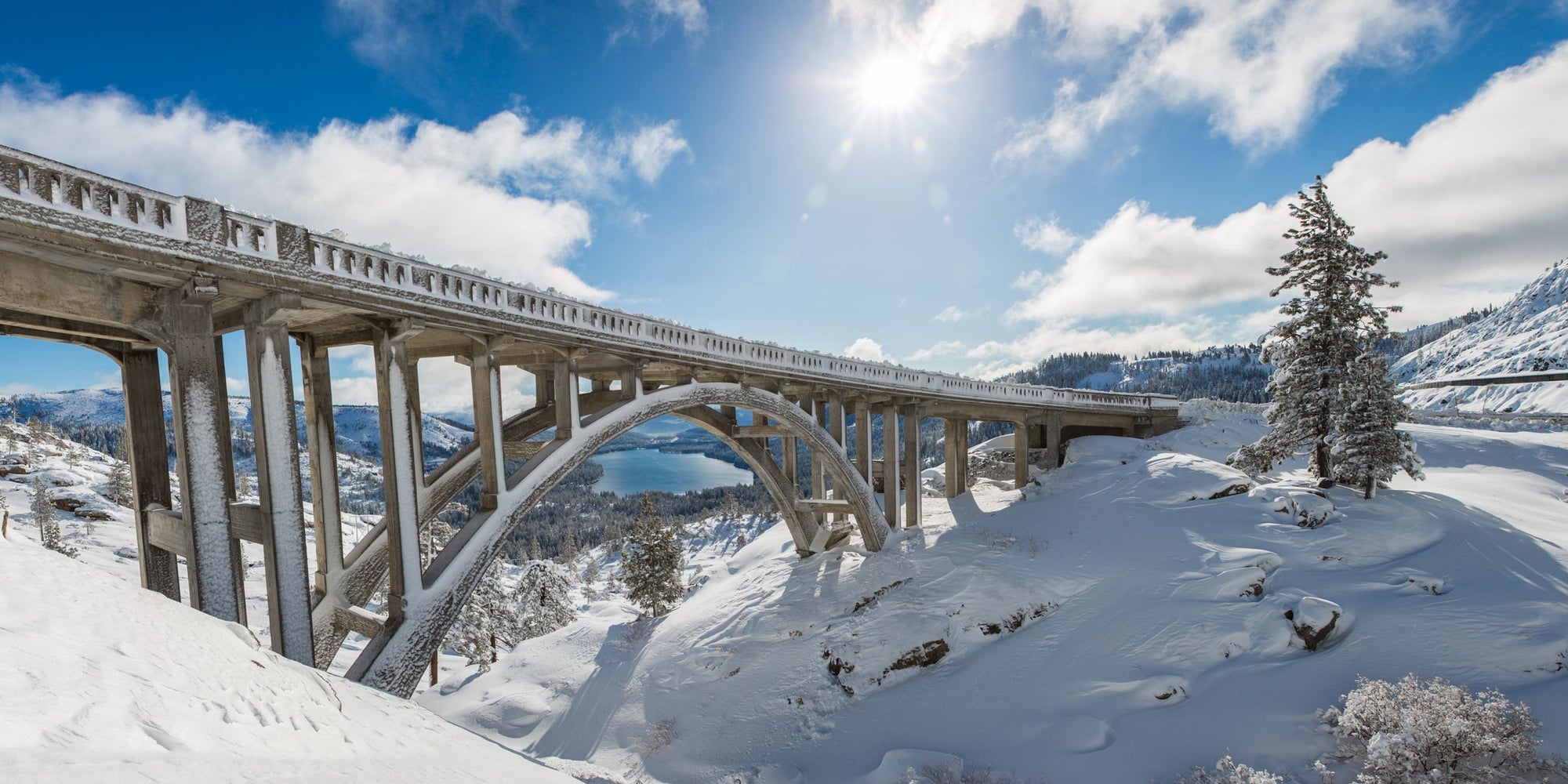 An arched bridge goes over a snowy gap above a lake.