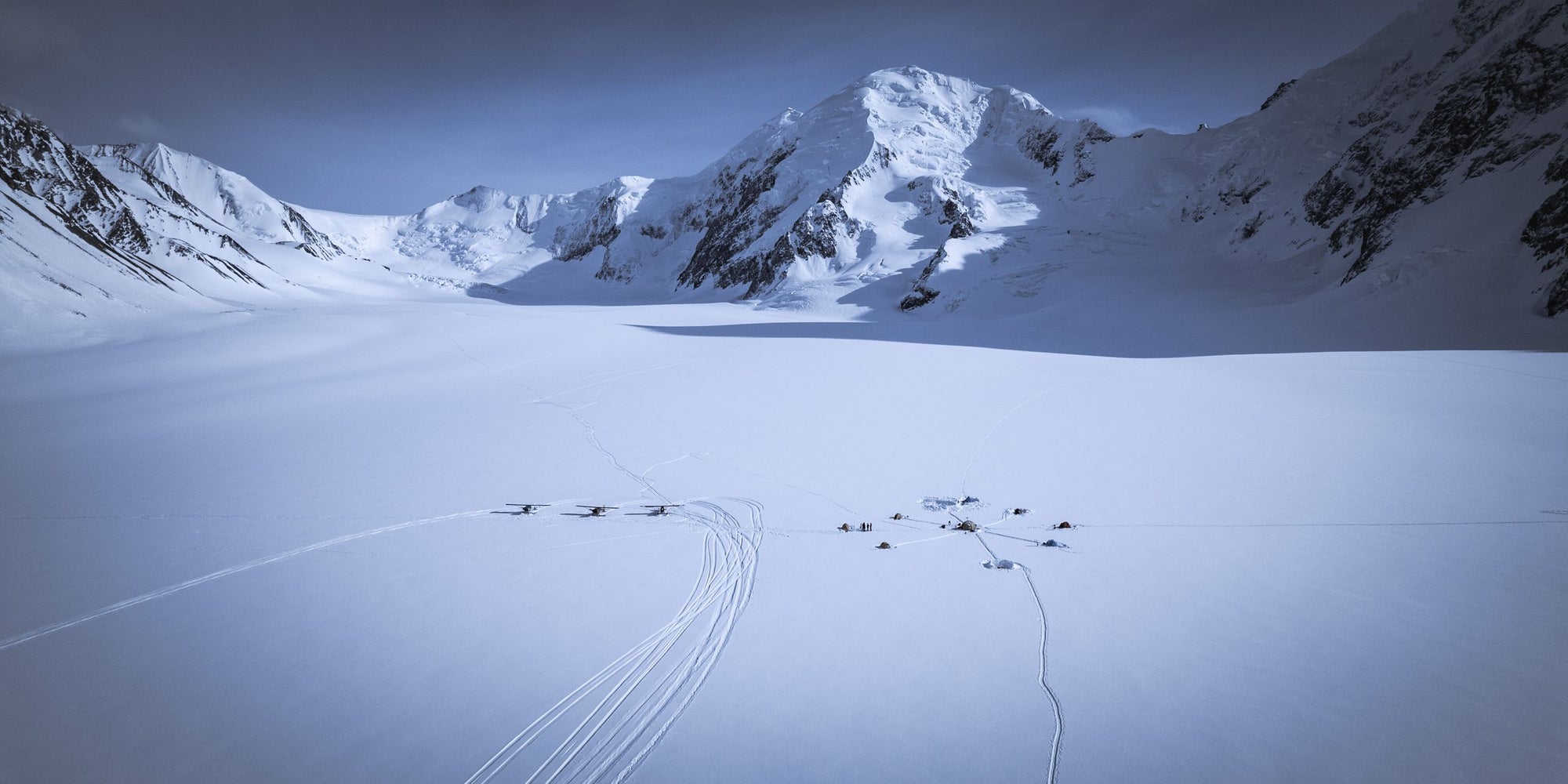 Three airplanes and one campsite sit on a snowy basin in the Alaska Mountains.