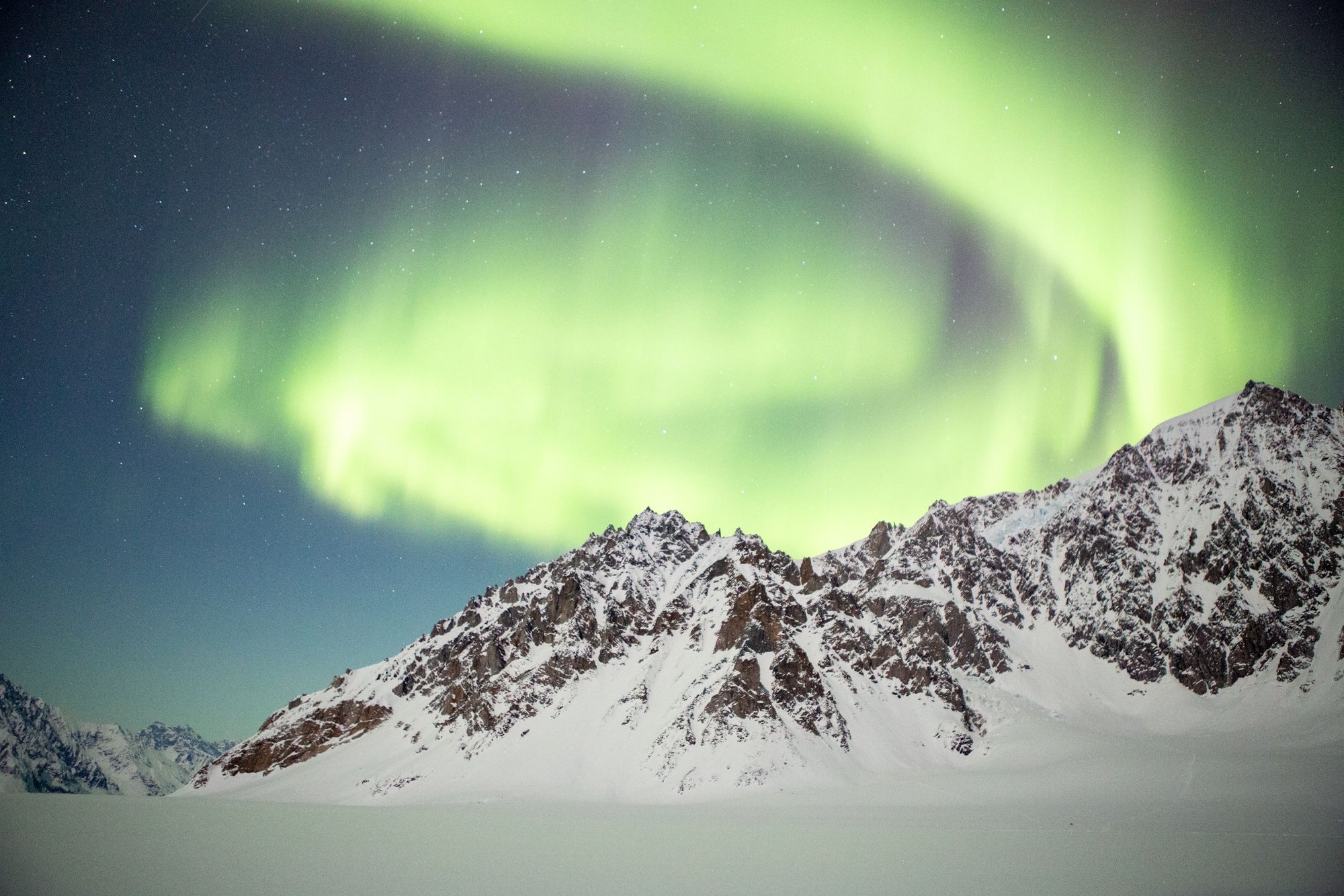 The Aurora Borealis shines above snow capped peaks.