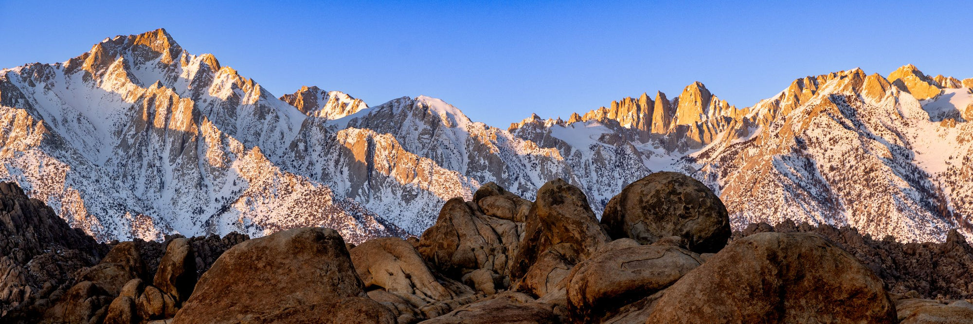 The sun sends golden highlights across the peaks of the Alabama Hills.