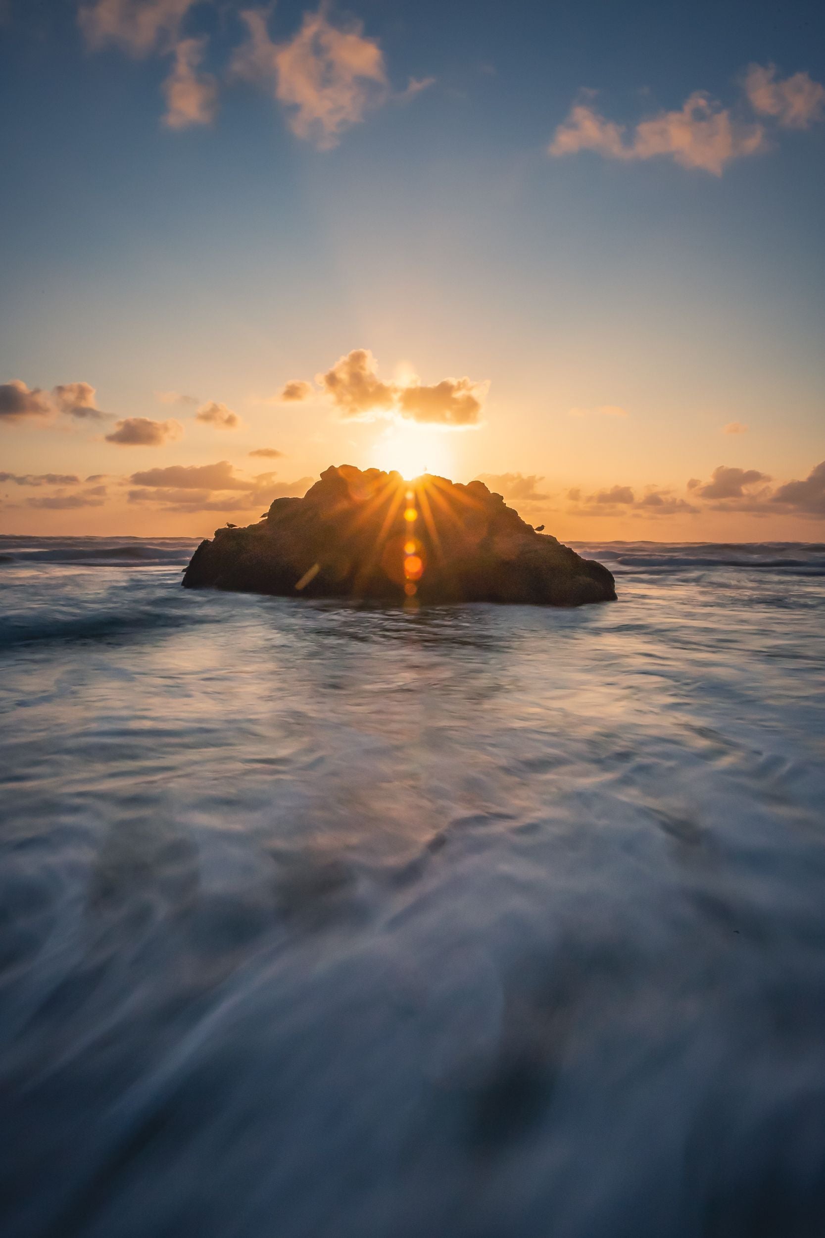 The sun sets behind a rock as it is lapped by the tides of the Oregon coast.