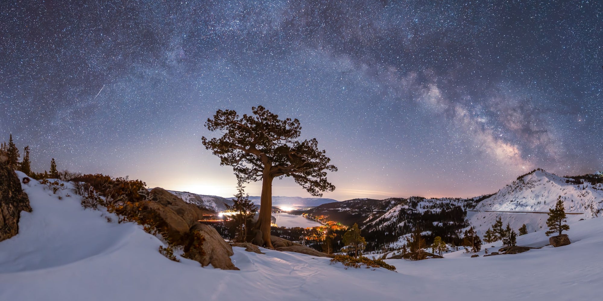A singular Juniper Tree sits below an arching Milky Way above Donner Lake and the town of Truckee, Ca.