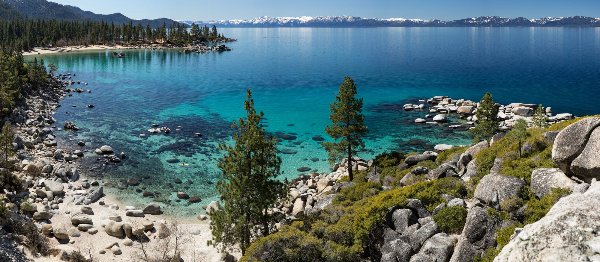 Snow capped peaks pine trees surrounding the turquoise waters of Lake Tahoe.
