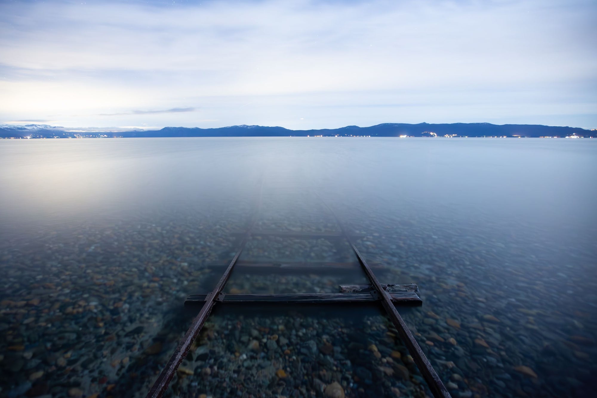 A set of train tracks disappear into a lake.