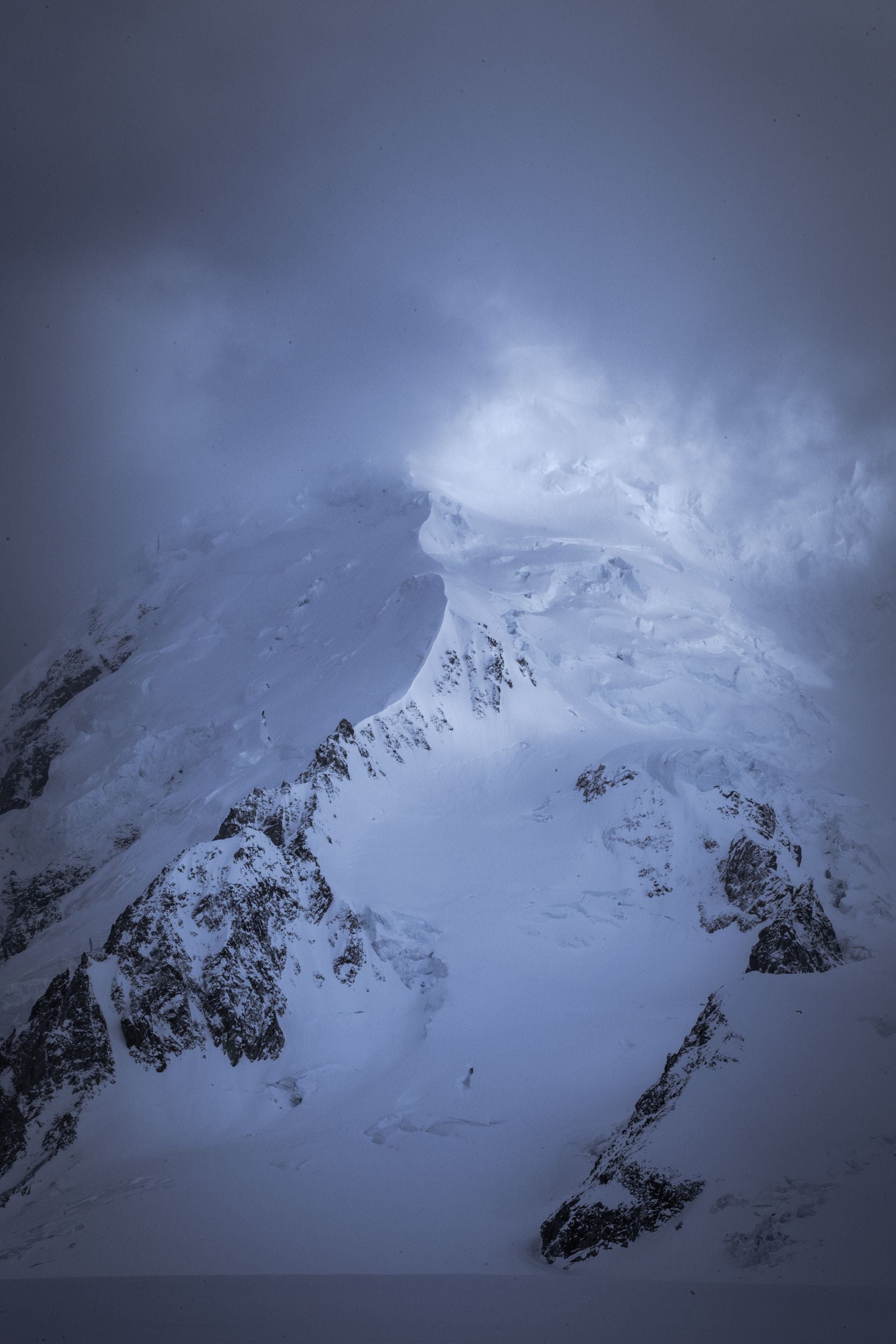 Fog and clouds hide a snow covered mountain peak and its ridge.