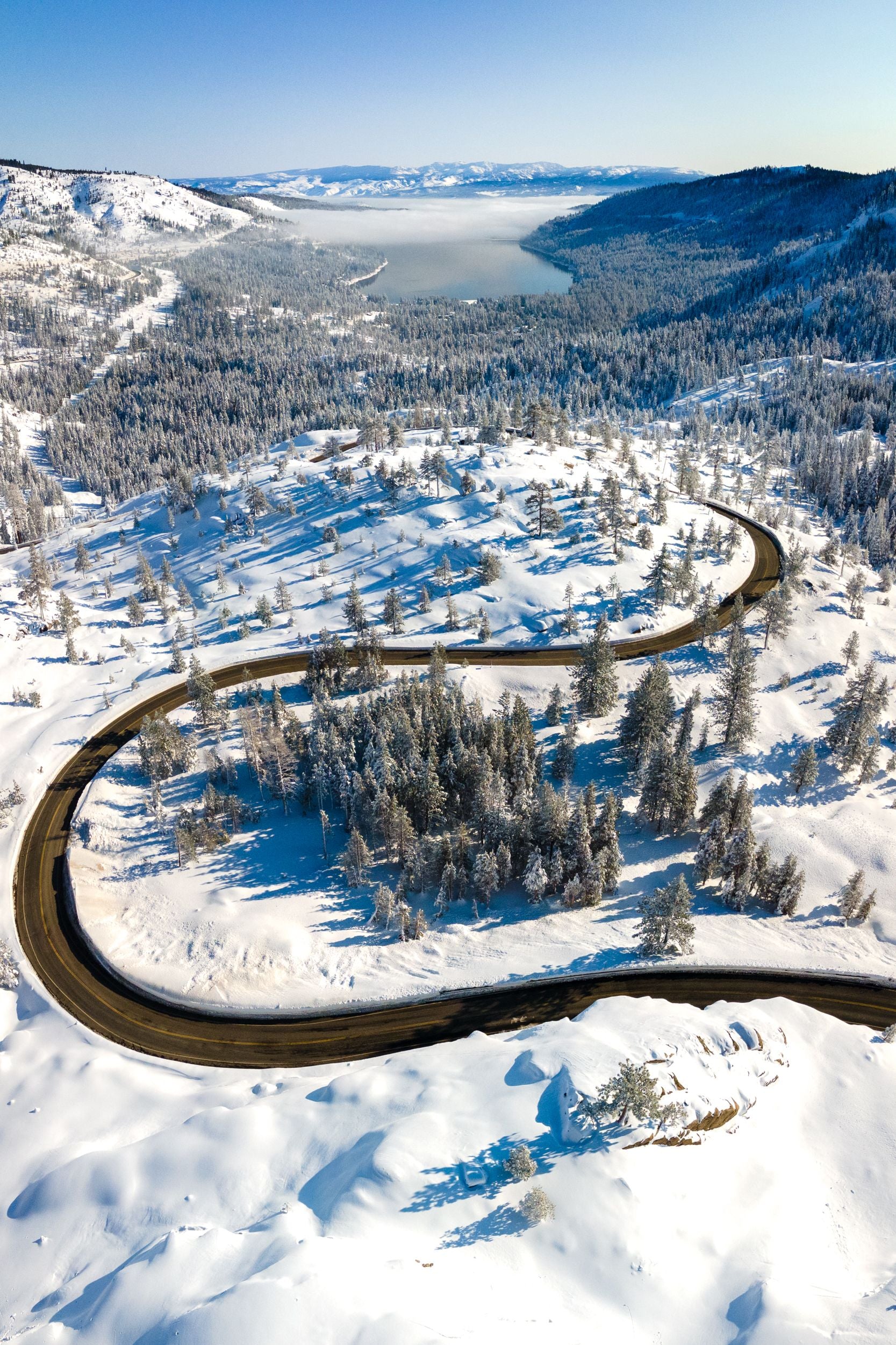 Old 40 Highway winds through snow covered hills towards a fog laden Donner Lake.
