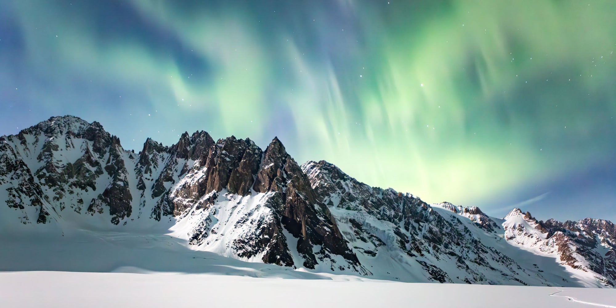 The green and blue lights of the Aurora Borealis sit above jagged peaks in Alaska.