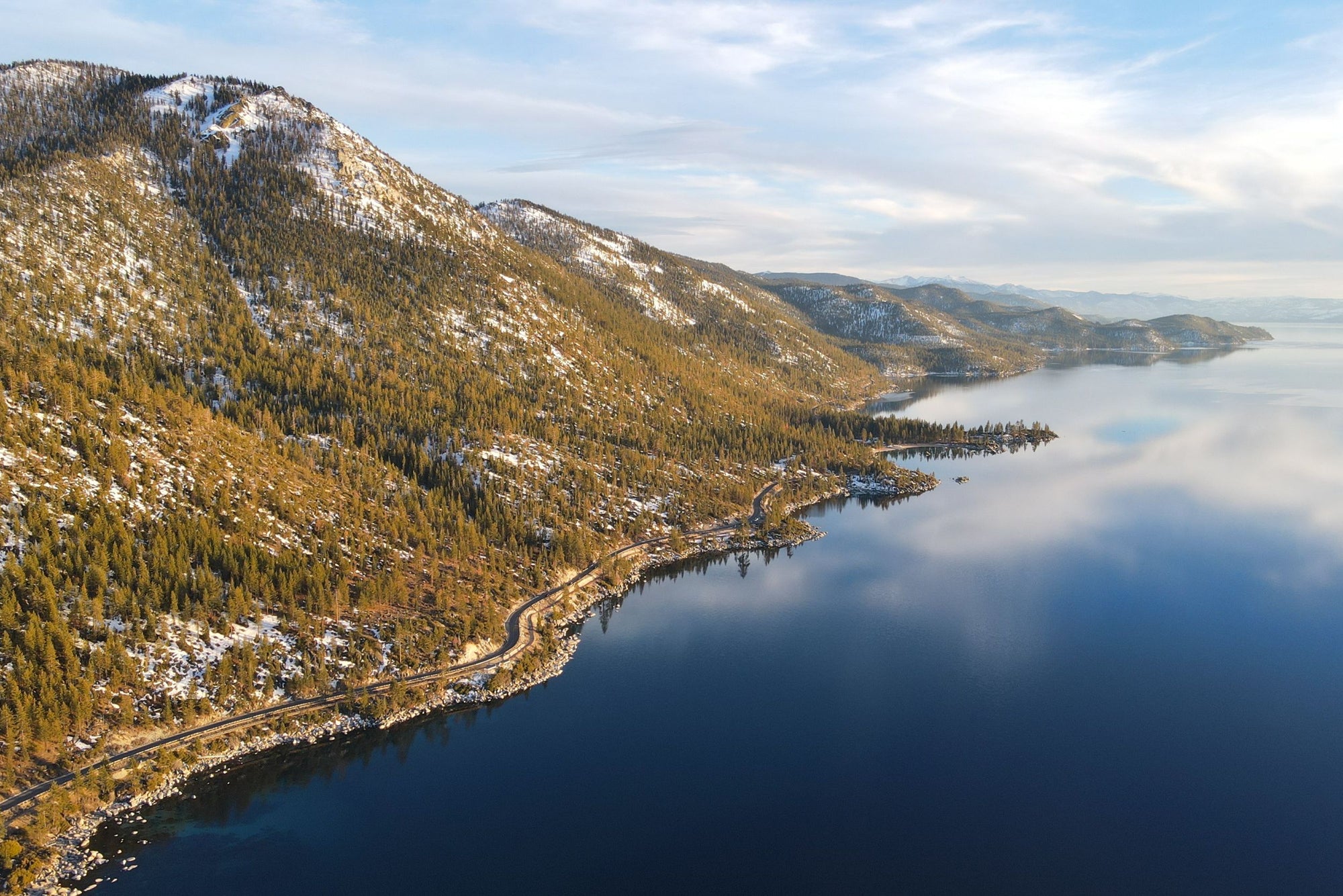 The blue water of Lake Tahoe hugs the shoreline of a treelined hillside.