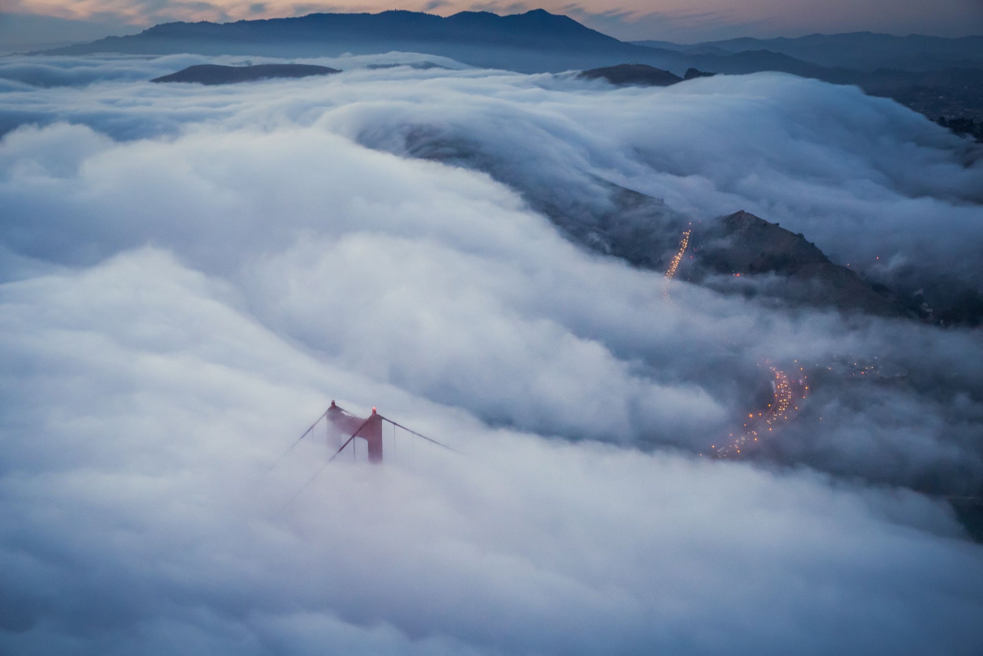 Fog blankets the Golden Gate Bridge as traffic winds down the road below.