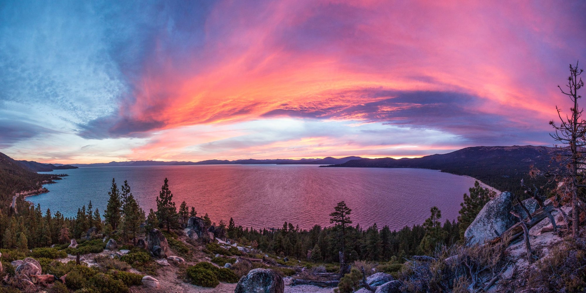 A pink, purple and blue sunset above Lake Tahoe with granite rocks and pine trees.